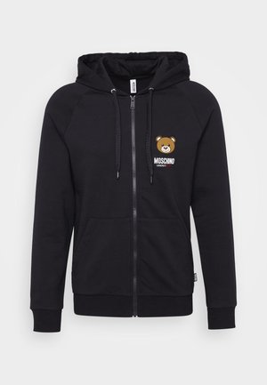 Black zip-up hoodie made of soft fabric. Features a bear graphic on the left chest and front pockets. Ribbed cuffs and hem.