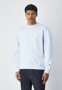 Sudadera azul claro hecha de una tela suave, presenta un cuello redondo, puños acanalados y un pequeño logo bordado en el pecho.