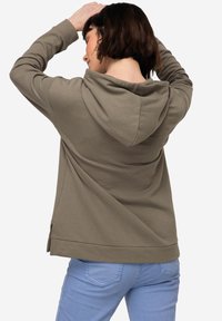 Khaki hoodie med avslappnad passform, med en dragsko i huvan och sidofickor, i kombination med ljusblå jeans. Mjuk textur av tyget synlig.
