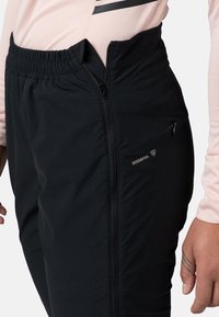 Pantalons noirs avec taille élastique, poche zippée et matière extensible. Présente un marquage visible et un design élégant et fuselé.