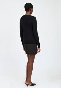 Suéter negro de punto con mangas largas y dobladillo acanalado, combinado con una falda verde oscura. La vista trasera muestra una silueta ajustada y un diseño sencillo.