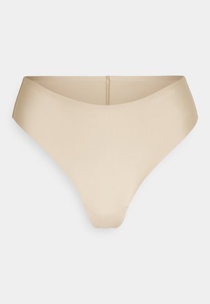 Nude thong underwear made of smooth, stretchy material. Features a low-rise cut and minimal stitching. Subtle logo accent on waistband.