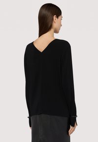 Maglietta nera a maniche lunghe con scollatura a V sul retro, realizzata in materiale morbido. Presenta maniche con polsini e dettagli in metallo.