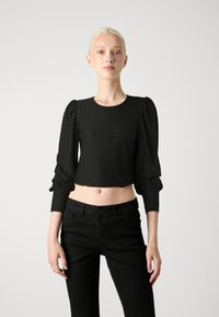 Top negro corto con mangas largas abullonadas, patrón texturizado y escote redondo, combinado con jeans negros de tiro alto.