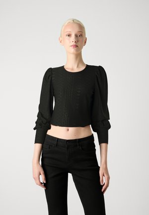 Sort croppetopp med lange puffermer, strukturert mønster og rund hals, kombinert med svarte høyt beltejeans.