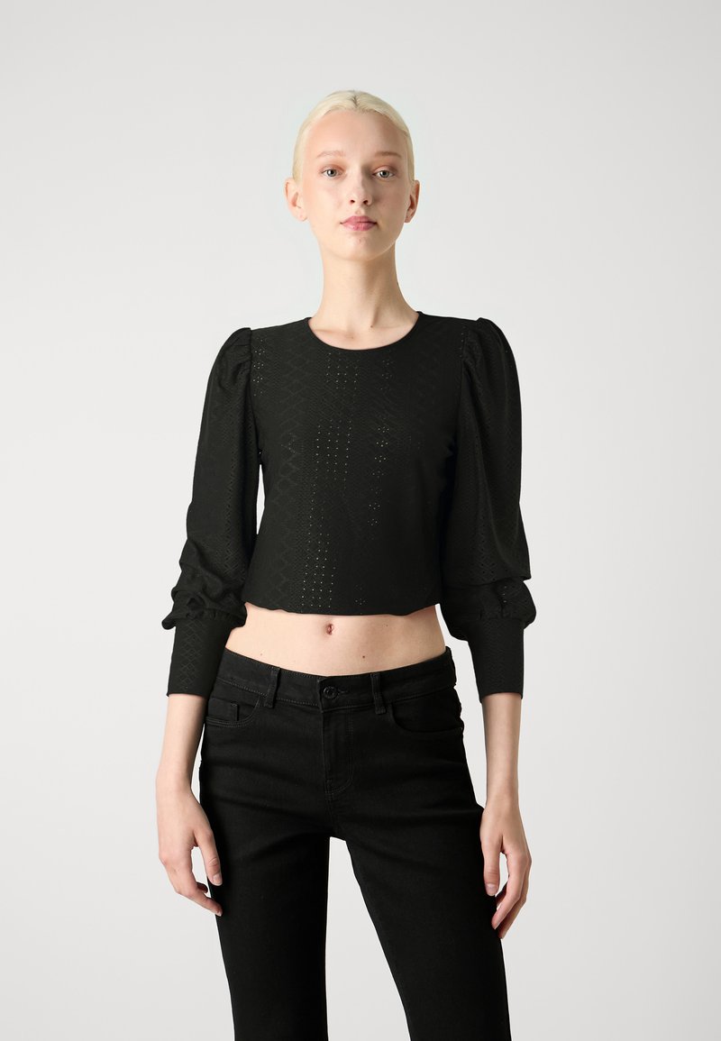 Top negro corto con mangas largas abullonadas, patrón texturizado y escote redondo, combinado con jeans negros de tiro alto.