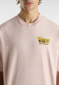 Helles rosa Baumwoll-T-Shirt mit Rundhalsausschnitt, das ein gelbes und schwarzes „Vans Off The Wall“-Logo in Stickerei auf der Brust aufweist. Einfaches Design, kurze Ärmel.