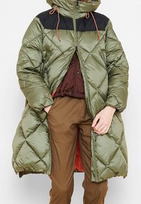 Cappotto imbottito verde oliva con spalle nere, chiusura con zip e cappuccio. Presenta un motivo trapuntato e cordini al collo.