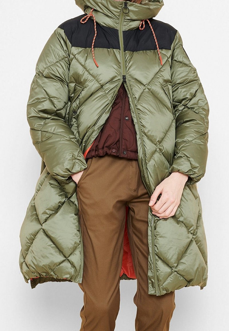 Cappotto imbottito verde oliva con spalle nere, chiusura con zip e cappuccio. Presenta un motivo trapuntato e cordini al collo.