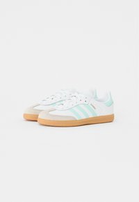 Zapatillas blancas con rayas verde menta, puntera de ante, cordones blancos y suela de goma. El diseño presenta un perfil bajo y un cuello acolchado.