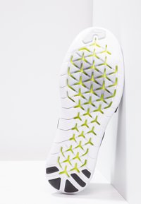 Sole bílé sportovní obuvi s trojúhelníkovými detaily v limetkově zelené barvě a černými protiskluzovými sekcemi, umístěná na pozadí s bílými rohy.