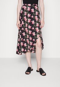 Saia midi floral em preto com flores rosas e folhas verdes; apresenta uma fenda lateral e uma cintura ajustada. Combinada com sandálias pretas de slide.