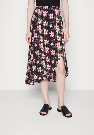 Saia midi floral em preto com flores rosas e folhas verdes; apresenta uma fenda lateral e uma cintura ajustada. Combinada com sandálias pretas de slide.
