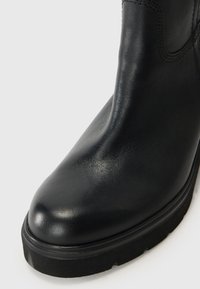 Zwarte leren enkelboot met een ronde neus, een gladde textuur en een dikke zwarte rubberen zool. Kenmerkt zich door minimale stikseldetails.