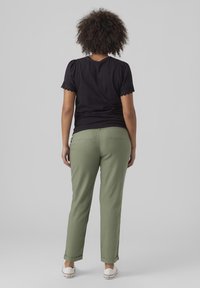 Svart kortärmad topp med vågig kant, ihopparad med olivgröna tapered byxor och vita låga sneakers, visad bakifrån.