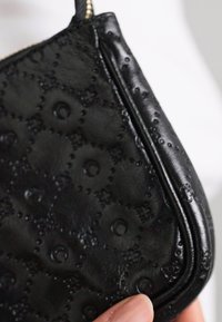 Clutch din piele neagră cu un model floral texturat, închidere cu fermoar și formă curbată. Suprafață netedă cu accente subtile în relief.
