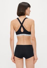 Fekete sportmelltartó keresztpántokkal és kulcslyuk részlettel, amelyet a sima elasztikus derékszíjjal ellátott fekete rövidnadrággal párosítottak.