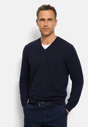 Maglione a V color navy realizzato in materiale morbido, con maniche lunghe e silhouette aderente, abbinato a pantaloni scuri e cintura.