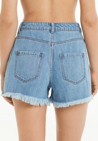 Shorts de mezclilla en azul claro con un dobladillo deshilachado, que cuentan con dos bolsillos traseros y una cintura ajustada. El material tiene una textura suave y lisa.