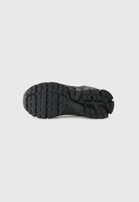 Semelle de chaussures de sport noire en caoutchouc texturé, avec un motif de carrés et de rectangles pour une meilleure adhérence et traction.