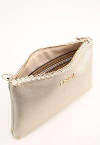 Metallic guld clutchtaske med tekstureret overflade, lynlås lukning og beige foring. Har indvendige rum til organisering.