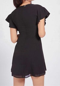 Schwarzes Kleid mit kurzen, gerafften Ärmeln, einem taillierten Oberteil und einem ausgestellten Rock mit transparentem Saum. Rückwärtiger Reißverschluss sichtbar.