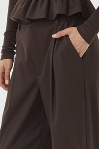 Brown wide-leg trousers with a smooth texture, featuring front pleats and a side pocket, paired with a matching layered top.