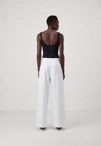 Mono negro con tirantes anchos combinado con pantalones blancos de tiro alto y pierna ancha, visto desde la parte de atrás.