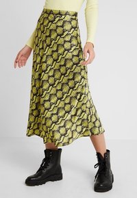 Keltainen ja musta käärmeennahkakuosis midi-hame, jossa on valuva design, yhdistettynä mustiin nauhakenkiin.