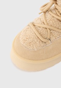 Baskets beige texturées avec un dessus en molleton doux, des accents en daim et des lacets plats. Présente une semelle en caoutchouc épaisse et des œillets en métal pour les lacets.