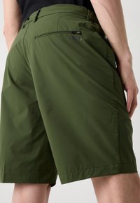 Shorts verts en tissu léger, dotés d'une poche arrière avec fermeture éclair, et d'une texture lisse avec une coupe ajustée.
