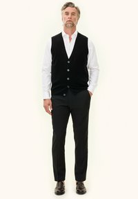 Zwarte gebreide vest, witte overhemd met knopen, zwarte broek, bruine schoenen. Strakke lijnen, klassieke pasvorm, eenvoudig ontwerp en neutrale kleuren.