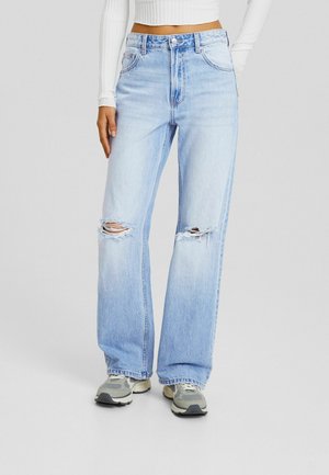 Light blue high-waisted jeans with a relaxed fit, featuring frayed rips on the knees and a faded texture. Paired with gray athletic shoes.