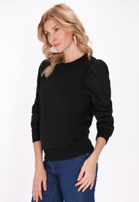 Felpa nera con maniche a sbuffo testurizzate e orlo a coste, abbinata a jeans skinny blu. Design semplice e casual senza motivi o adornamenti.