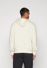 Cream hooded sweatshirt with ribbed cuffs and hem, made from soft fabric. Features a large hood and relaxed fit.