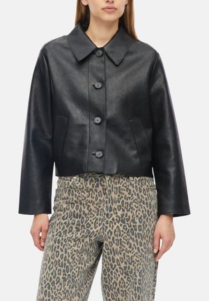 Donna che indossa una giacca corta in pelle nera con bottoni e maniche larghe e pantaloni beige a stampa leopardata a vita alta.