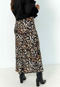 Leopard print midi skirt with a flowing design, featuring shades of brown, black, and cream. Paired with black heeled boots.