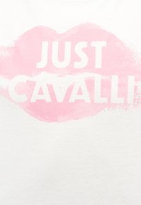 Ροζ σημάδι κραγιόν με τις λέξεις "JUST CAVALLI" τυπωμένες με λευκά κεφαλαία γράμματα μέσα στο σχήμα χείλους σε λευκό φόντο.