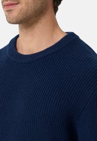 Dunkelblauer gerippt gestrickter Pullover mit weitem Rundhalsausschnitt und weicher Textur. Nahaufnahme des Kragens und des Schulterbereichs.