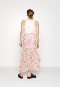 Jupe maxi florale en tissu rose tendre avec des motifs floraux orange et rouge, associée à un débardeur blanc et des sandales noires à enfiler.