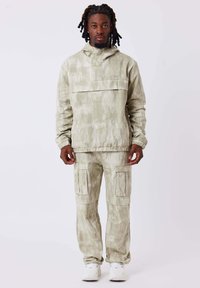 Giacca a pullover di colore verde chiaro, con texture, cappuccio e tasca frontale, abbinata a pantaloni cargo coordinati dotati di tasche laterali e polsini elasticizzati.