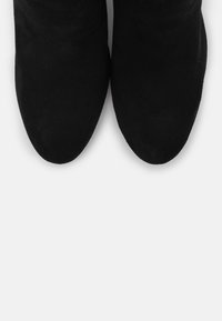 Botas de tobillo de ante negro con una textura suave, punteras puntiagudas y sin herrajes o patrones visibles, vistas desde arriba.