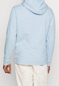 Sudadera azul claro hecha de una tela suave, con capucha ajustable, mangas largas y puños y dobladillo acanalados. La vista trasera muestra un diseño minimalista.
