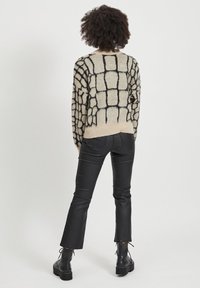 Maglione lavorato a maglia con un motivo a griglia nero su sfondo beige, indossato con pantaloni di pelle nera e robusti stivali neri.