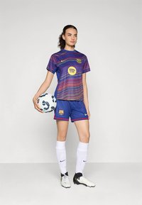 Dres FC Barcelona v purpurovej a modrej farbe s vlnkovým vzorom a logom Spotify; doplnený modrými nohavicami, bielymi ponožkami a futbalovými topánkami.