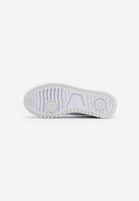 White athletic shoe outsole featuring a textured rubber surface with treading patterns and circular accents for grip.