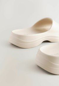 Hvide platformstræskere med en glat, mat tekstur, der har et buet design og en let hævning ved hælen. Ingen synligt hardware eller mønstre.