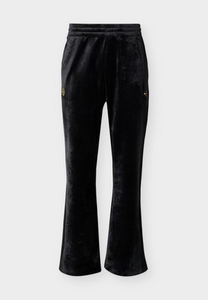 Pantalones deportivos de terciopelo negro con piernas acampanadas, cintura elástica y pequeños logos dorados en cada muslo sobre un fondo blanco liso.