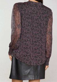 Blouse à manches longues en tissu transparent à motifs floraux noirs et roses, associée à une jupe en cuir noire avec un ourlet arrondi.