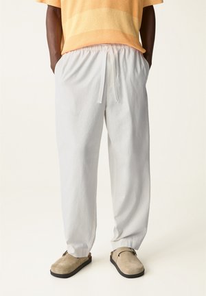 Pantalones blancos ligeros con cintura elástica y cordón. Combinados con zapatos de slip-on beige y una camiseta texturizada naranja.